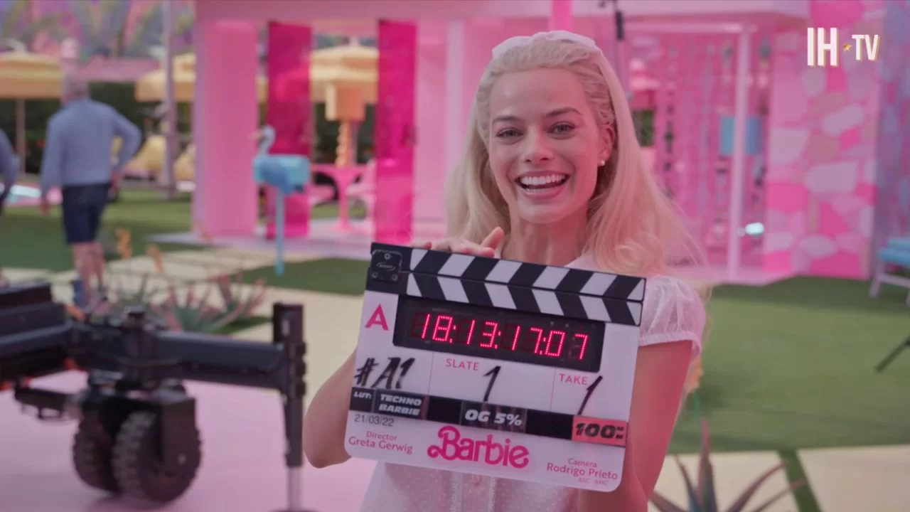 Margot Robbie sorridente segura a claquete de Barbie no set