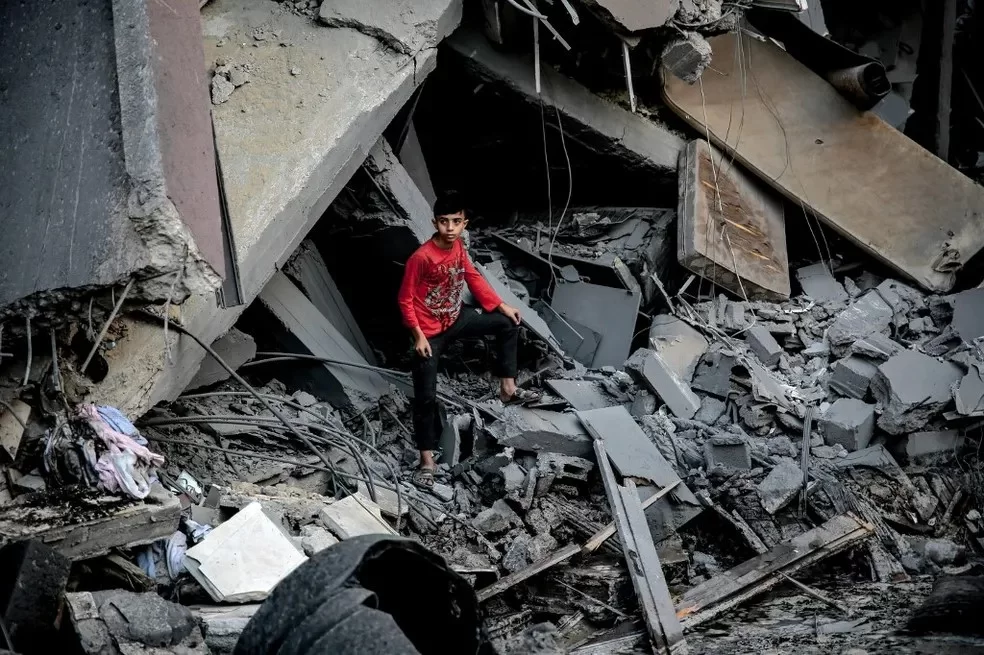 Menino palestino em frente a escombros de edifício após ataque israelense à Cidade de Gaza, em 26 de outubro de 2023