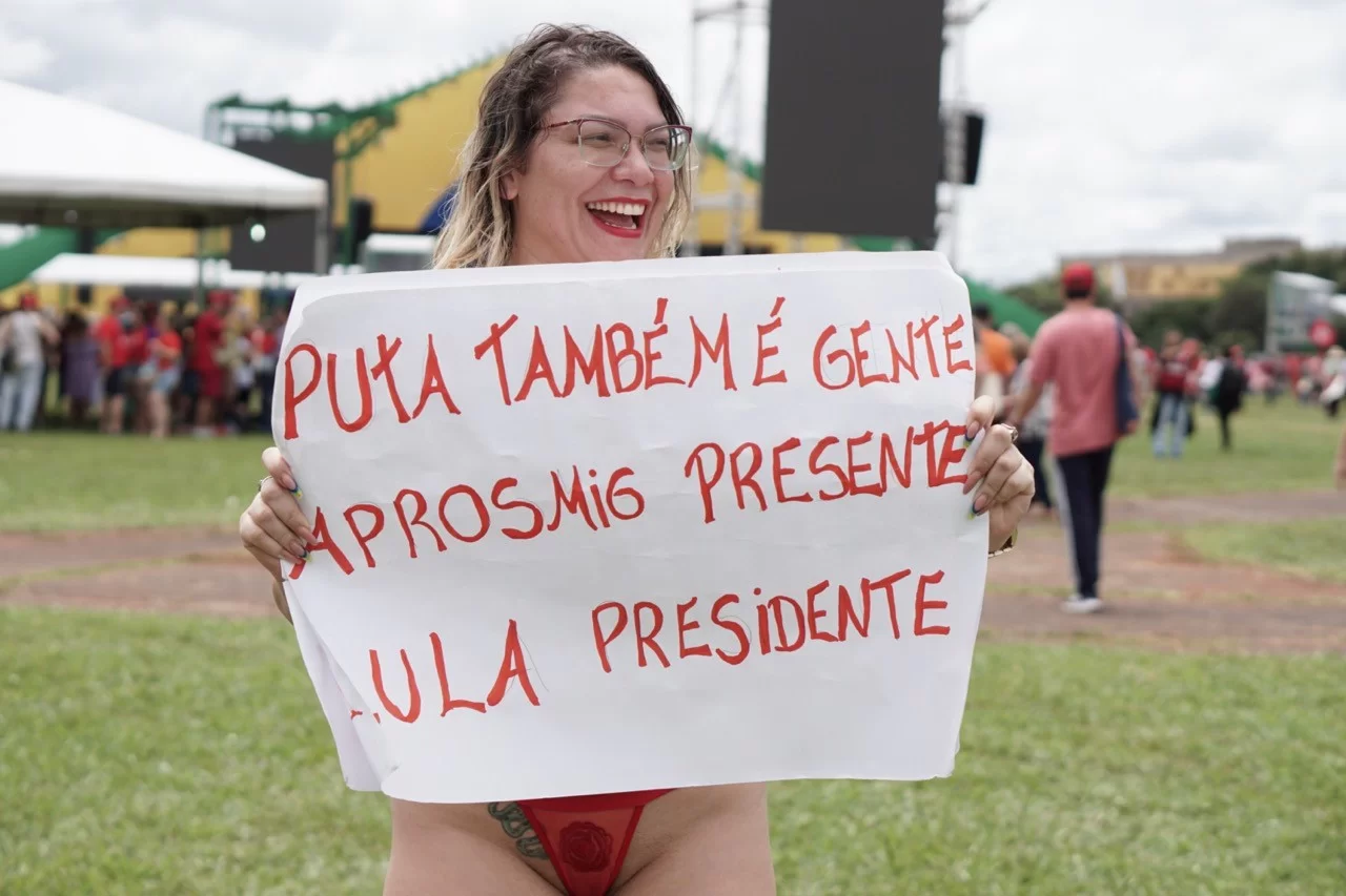 Mulher que seria Janja, segurando cartaz defendendo a prostituição