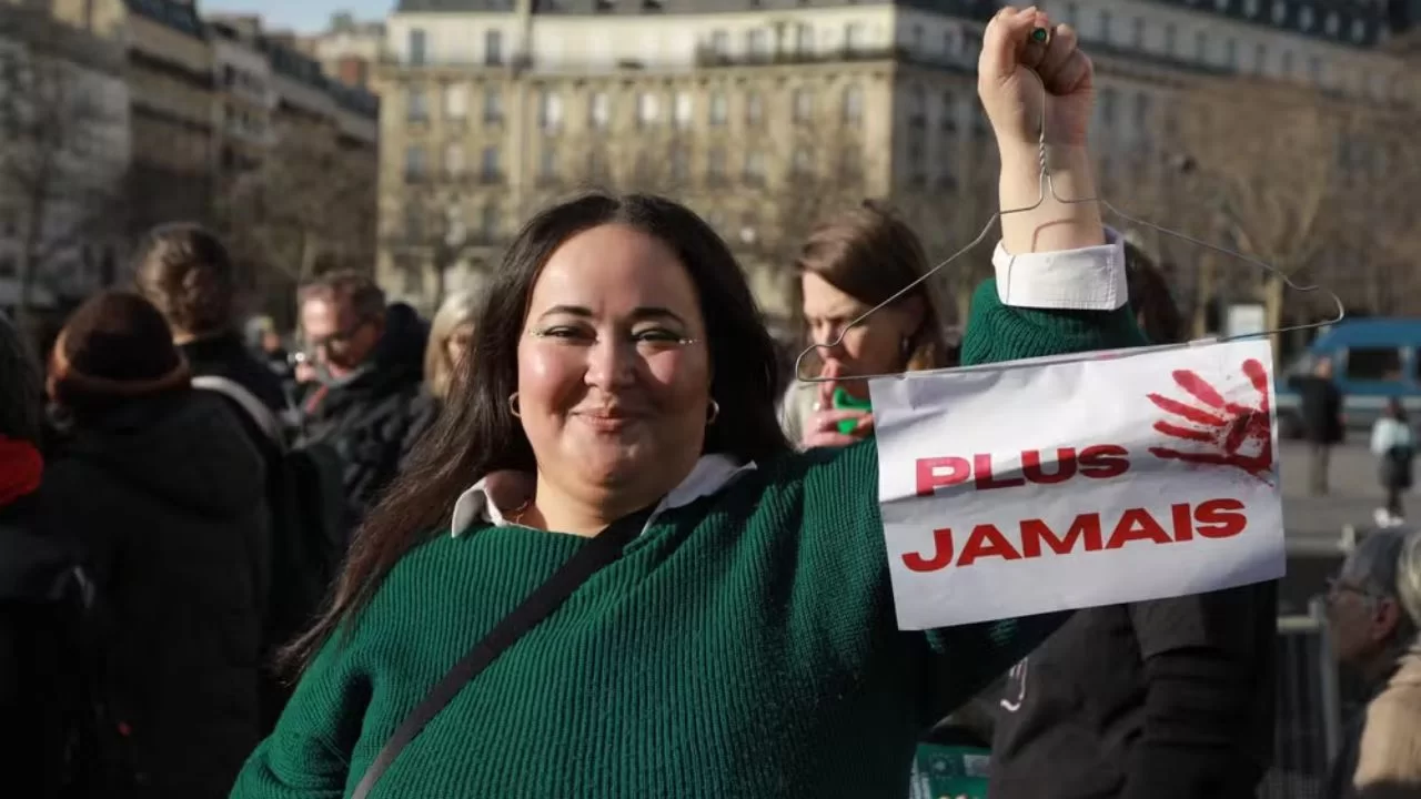 Manifestante a favor da inclusão de aborto na Constituição francesa ergue cartaz com cabide e frase 'Nunca Mais'. 