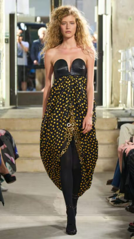 Modelo na passarela com vestido preto e bolinhas amarelas em estilo retrô